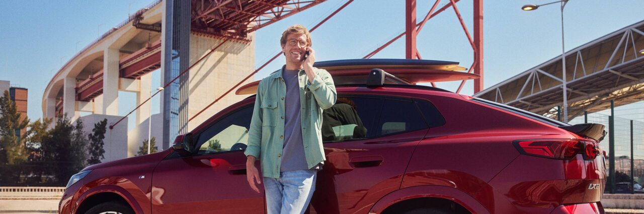 Man heeft een telefoon in zijn hand en leunt tegen zijn BMW aan.
